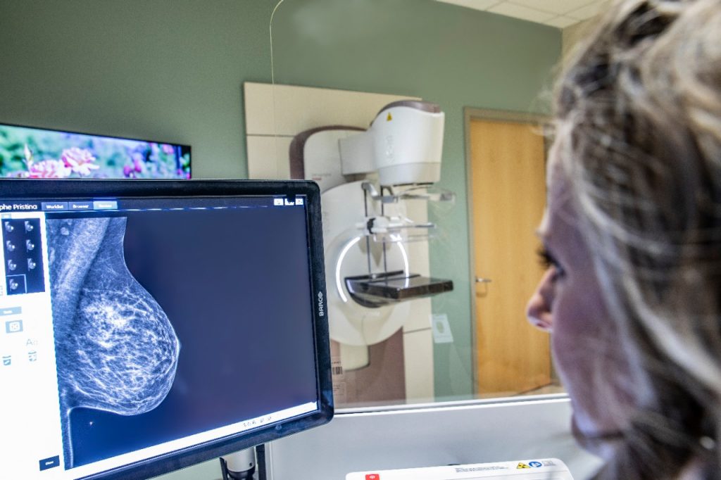 A medical professional at right looking at the image from a mammogram on a computer screen.