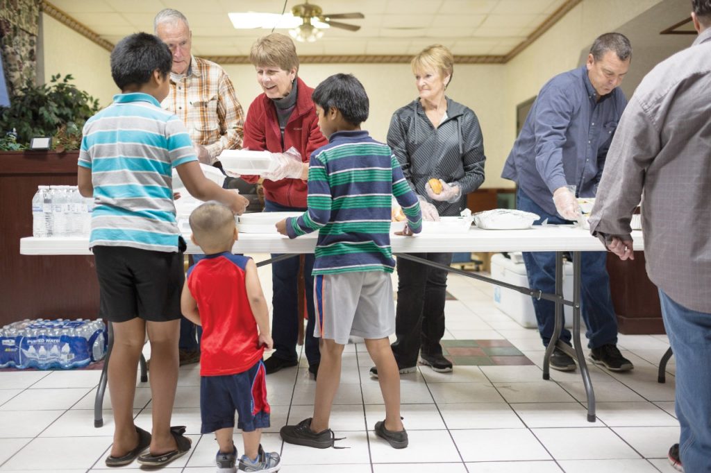 From left, Dale and Deb Bennett and Diana Hartung of Bland Chapel United Methodist Church offer boxed meals to a trio of boys as part of Mercy's outreach to the near-homeless at a motel in Rogers, Arkansas. (Permission granted from Catholic Health World, February 15, 2018
Copyright © 2018 by The Catholic Health Association of the United States.)
