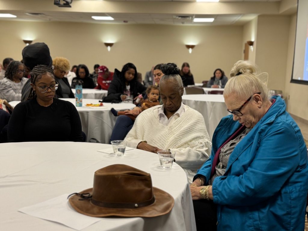 Erma Willis-Alford seated at a table with two other women, praying.