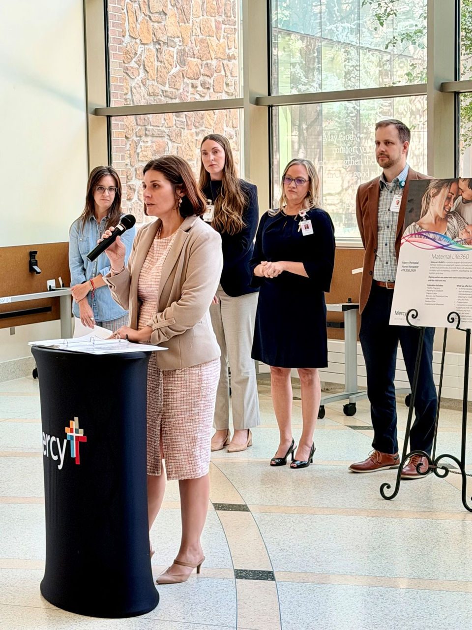 Woman speaks from podium with group gathered behind her.