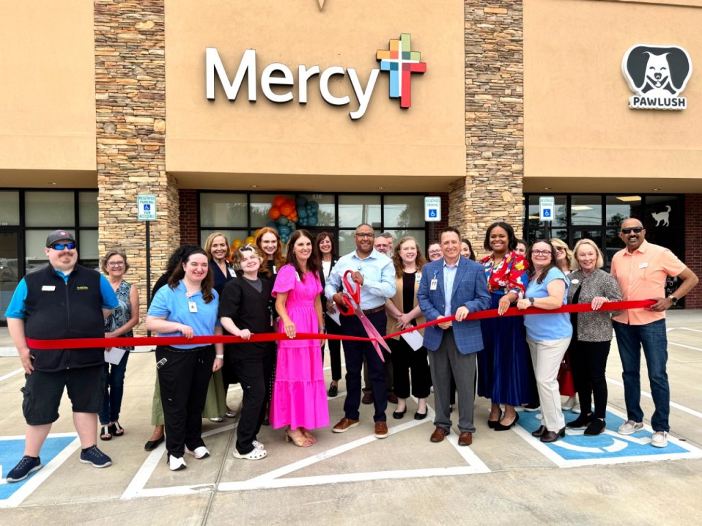 People standing behind a ceremonial red ribbon with oversize red scissors in front of a Mercy clinic.