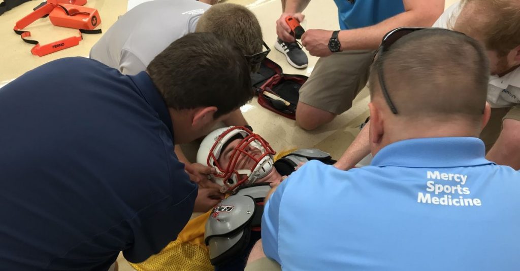 Mercy Sports Medicine athletic trainers practice how they would carefully remove a football player's gear if that student was injured during a game. The annual drill gets trainers ready at the end of each summer for the high school sports season ahead.