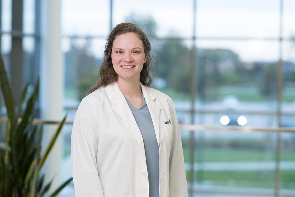 Dr. Hannah Kertz smiles as she poses in a white lab coat with a Mercy logo