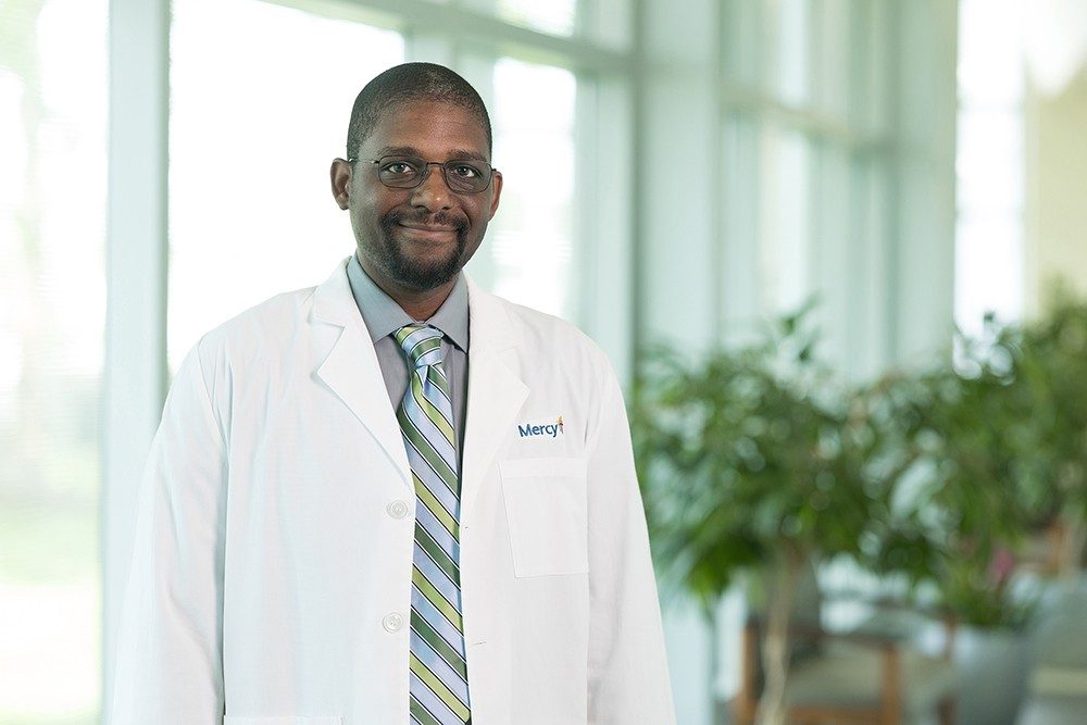 Dr. Jeremy Broadnax smiles in a poses photo while wearing a white lab coat with a Mercy logo