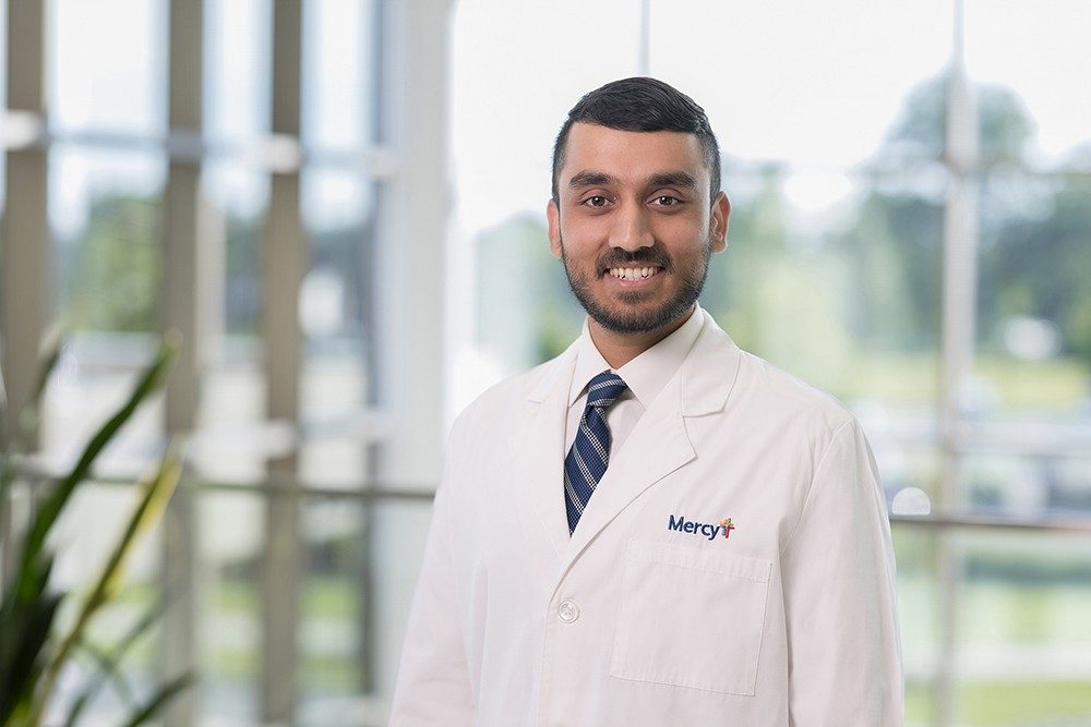 Dr. Rafid Rahman smiles in a posed photo while wearing a white lab coat with a Mercy logod rehabilitation