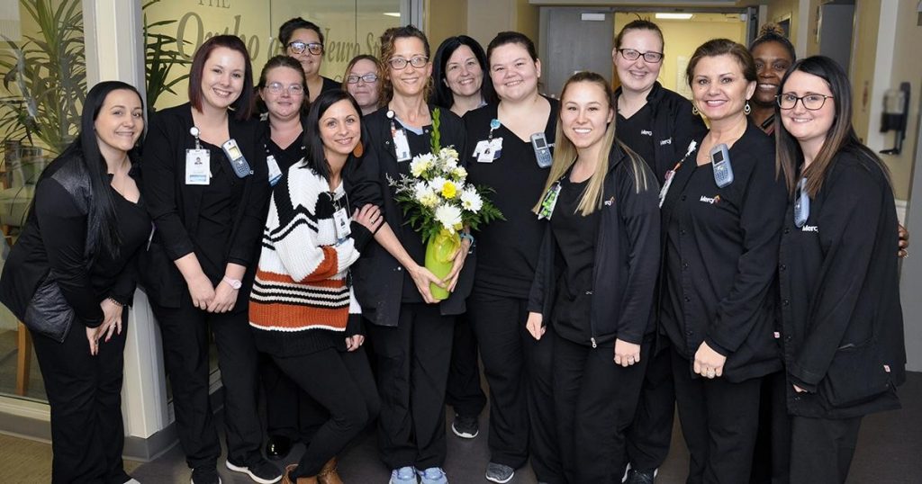 Kristin Wall, RN, (center, holding flowers) celebrates with her orthopedics co-workers after earning a DAISY Award for the extraordinary, compassionate and skillful nursing care she provides at Mercy Hospital South.
