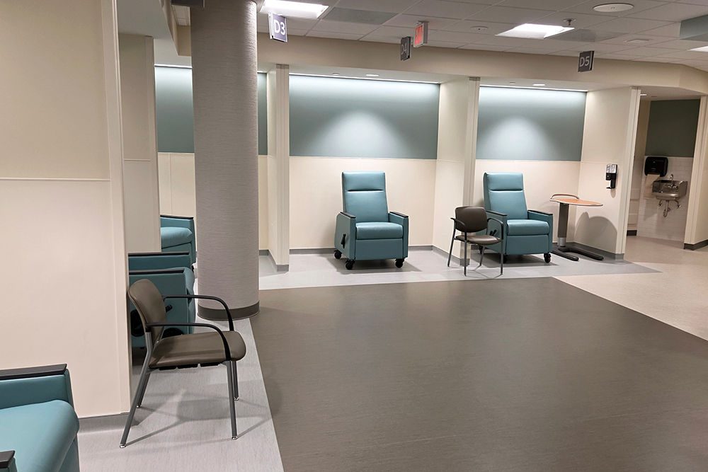 Several green recliners sit in individual bays in a healthcare setting.