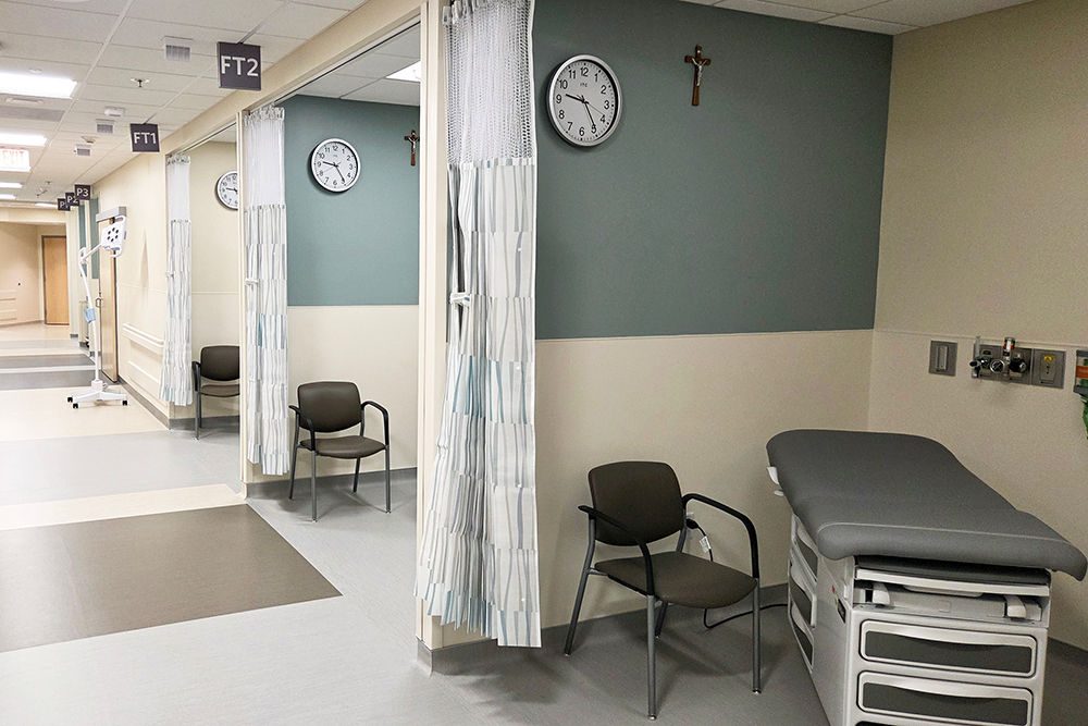Several bays are displayed with curtains open. A patient exam table and a chair are visible in the bay in the foreground.