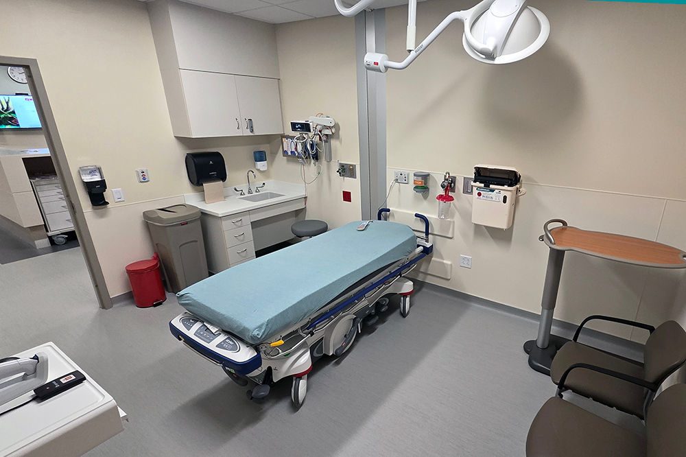 A patient care room with a bed, overhead light, sink and other medical equipment.