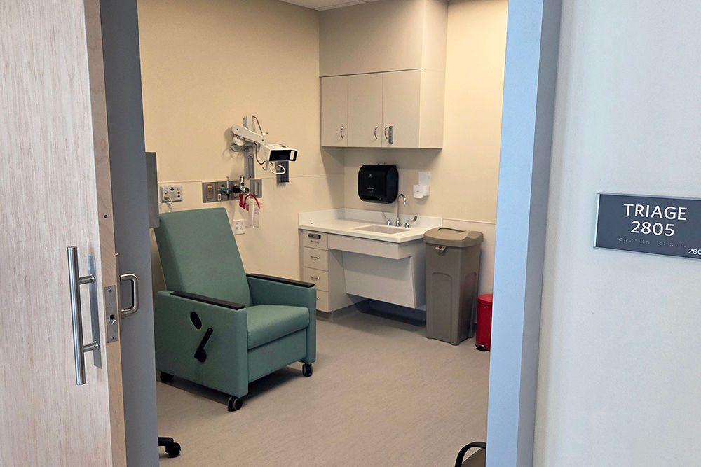 A triage room for patient care with a green chair with an open sliding door in the foreground.
