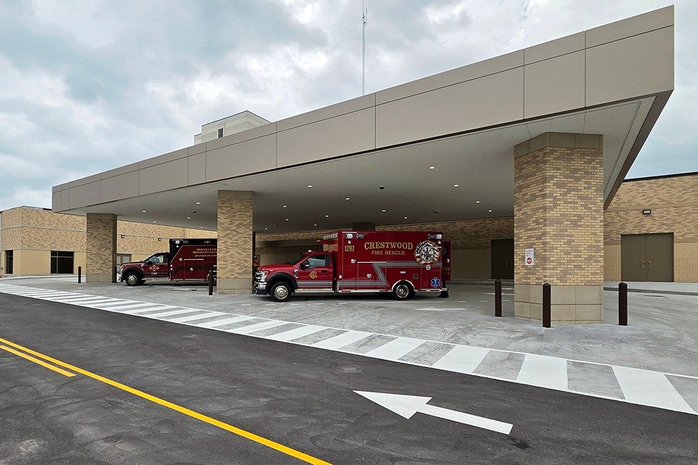 The exterior of an ambulance bay with a red Mehlville Fire District ambulance and a red Crestwood Fire Department ambulance park under the canopy.