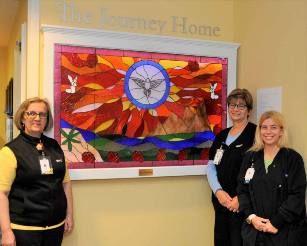 Three of Jim Good’s caregivers at Mercy Hospice South - de Greeff Hospice House gather at the stained glass window. They are, from left, home health aide Stanka Pupic; Christy Stellhorn, BSN, RN; and Jennifer Smelser, RN, supervisor of clinical nursing. 