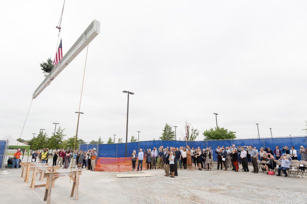 A crowd of about 100 people watch as a construction crane lifts the final steel beam into place for Mercy Hospital Northwest Arkansas' new seven-story tower.