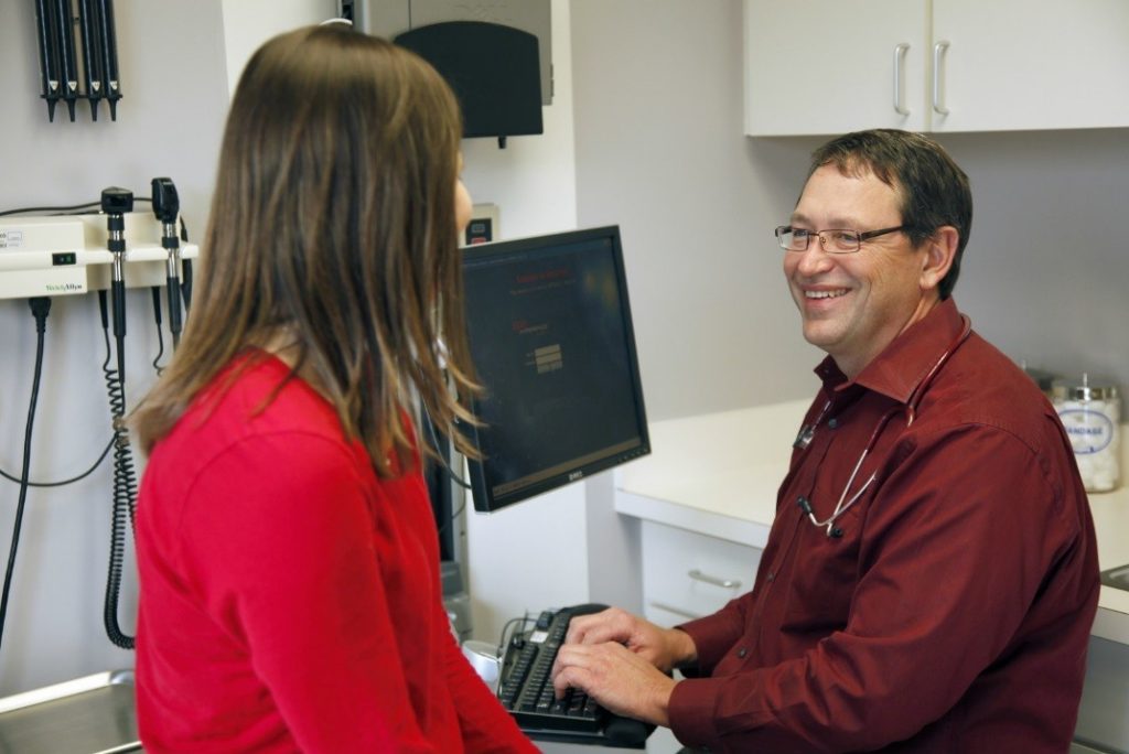 Dr. Arthur Hale visits with a patient, whose information is submitted into Epic in the room.
