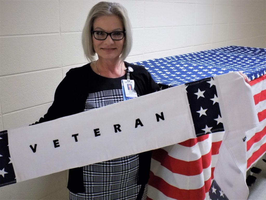 Crystal Hardy, a Mercy senior informatics analyst, holds the veterans sash used during Mercy Fort Smith's new Military Honor Walks. Hardy, who is a veteran, sewed the sash and the gurney cover seen behind her for use during the walks, which pay tribute to veterans and active military service members who pass away at the hospital. 

